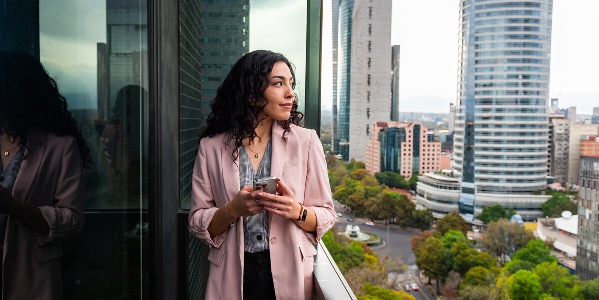 woman standing on balcony looking out, holding cellphone