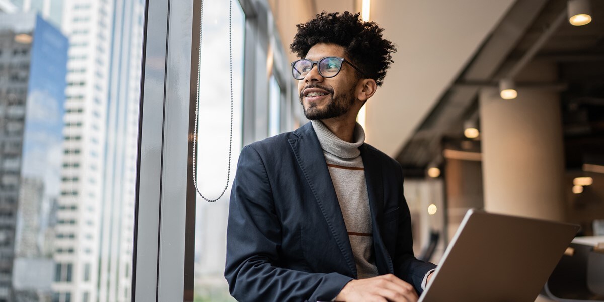 man sitting next to a window in the office, laptop in front of him