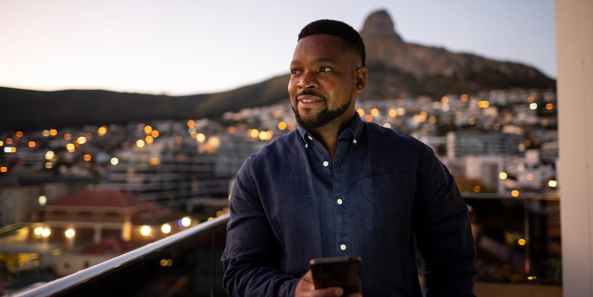 man standing outside, holding cell phone, city skyline behind him
