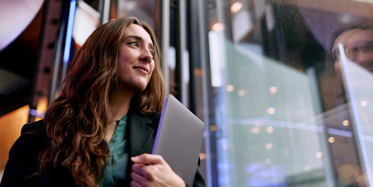 professional woman looking out window, holding laptop