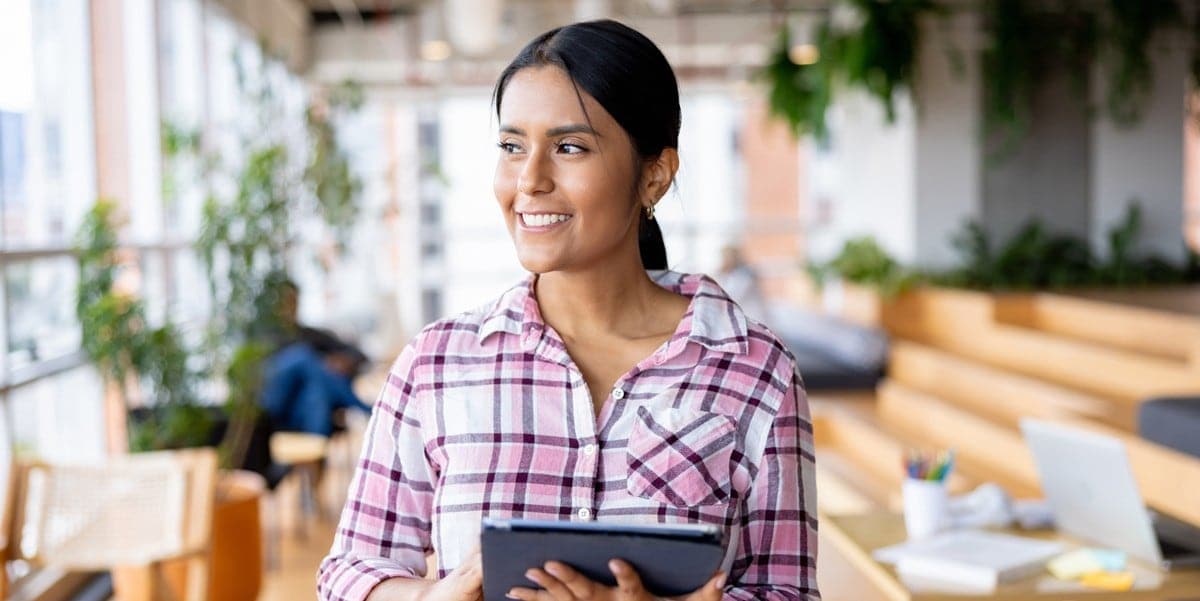 young professional woman smiling, in the office, holding tablet