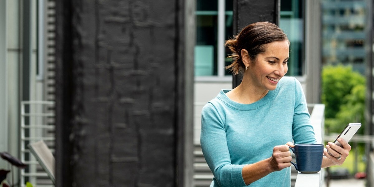 woman drinking coffee and reading on phone outside balcony